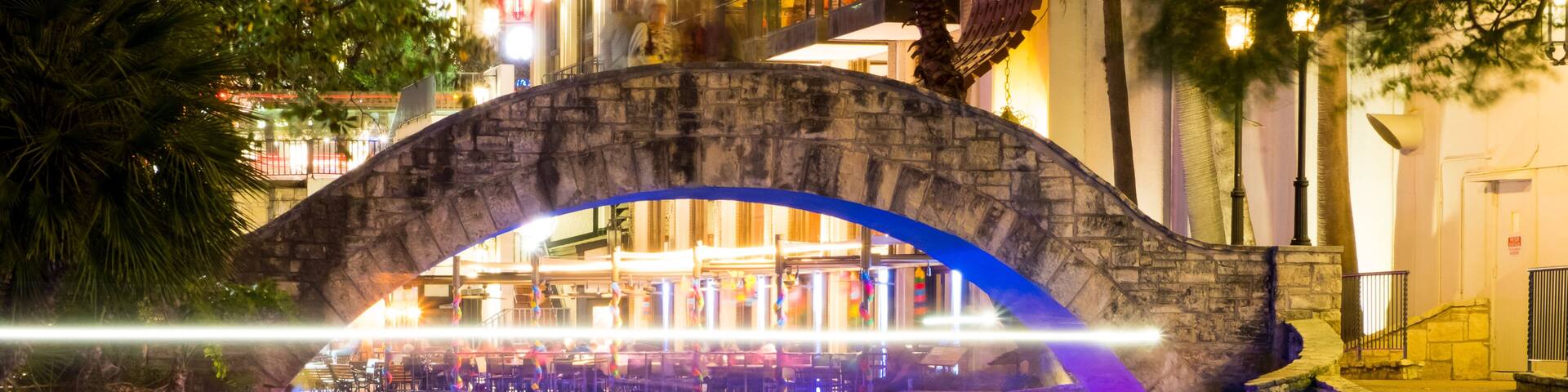 A stone bridge over a river with reflections of colorful lights.