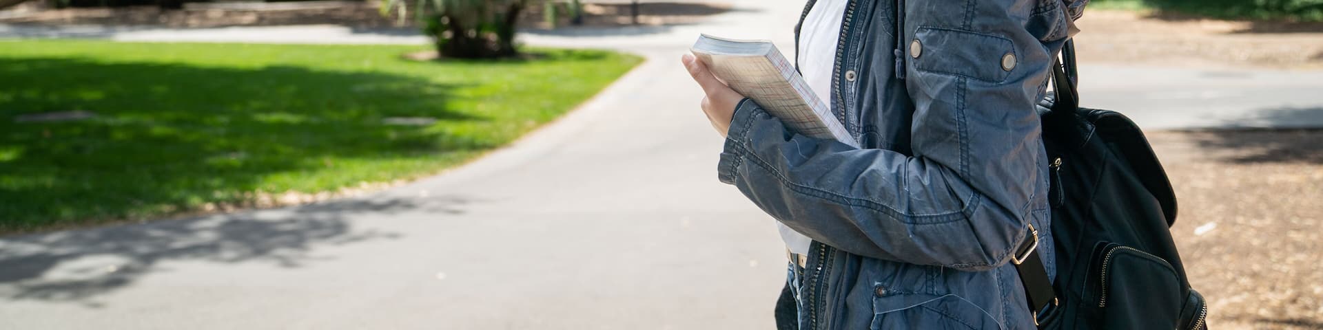 portrait of cheerful asian Korean female international student carrying book and looking at camera with smile against background of school campus and hoover tower in California usa