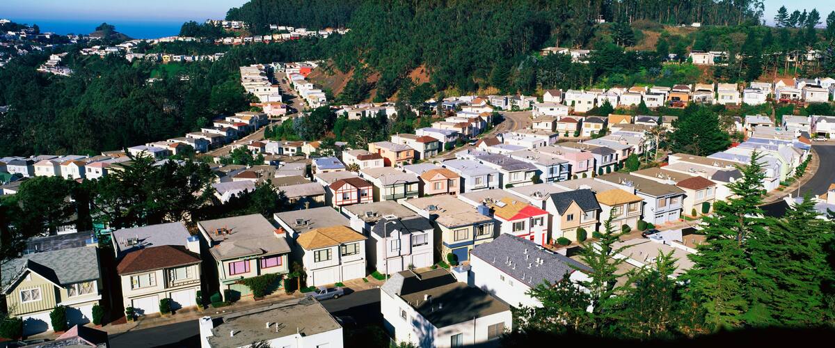 These are houses lined up in rows. They form a pattern and show urban congestion in housing. This is the view from Twin Peaks Mountain. There are green trees interspersed between the houses.
