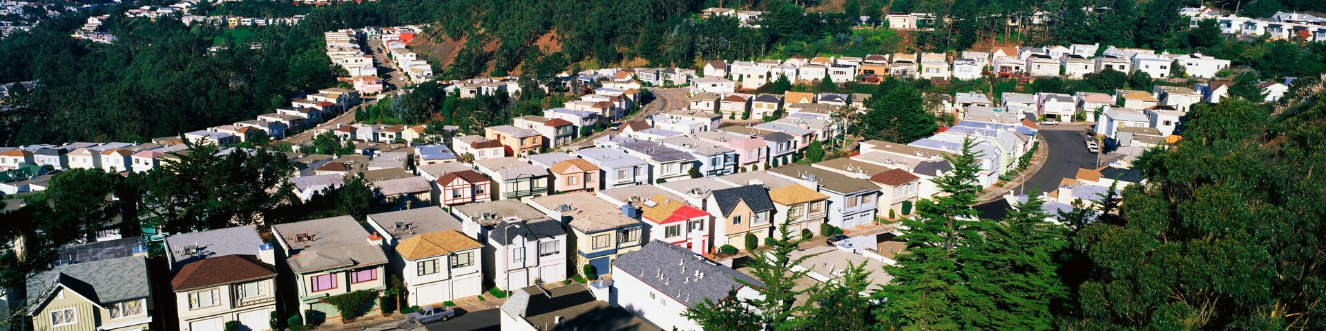 These are houses lined up in rows. They form a pattern and show urban congestion in housing. This is the view from Twin Peaks Mountain. There are green trees interspersed between the houses.
