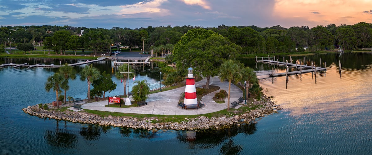 Aerial panorama of Mount Dora Lighthouse on Lake Dora at sunset with boat docks and palm trees in Florida. USA. May 18, 2023.