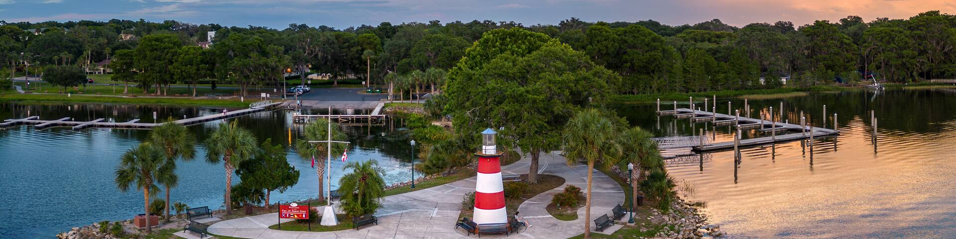 A lighthouse on a small island surrounded by water, with a dock and benches nearby.