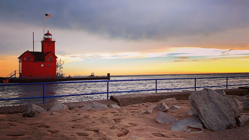 A red lighthouse by the sea during sunset.