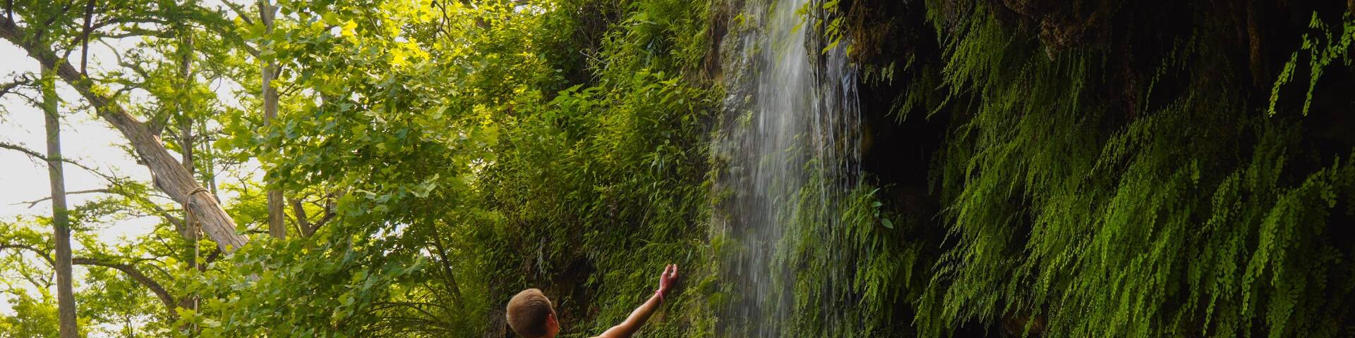 A waterfall in a forested area with a person standing on rocks.