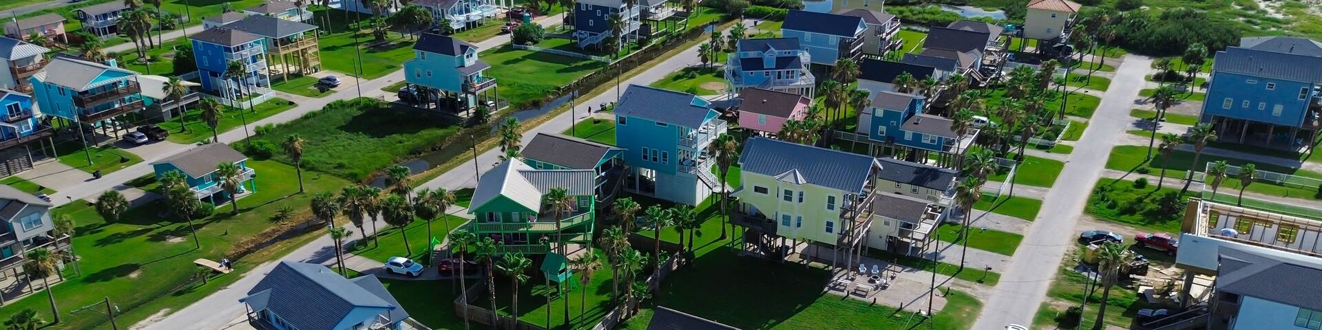 Panorama view grid of stilt vacation homes with grassy vacation land, Galveston, TX. Green space and paved drives support drainage, aesthetics, reflecting thoughtful coastal-suburban integration