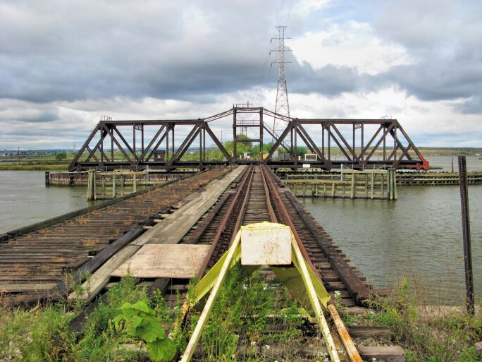 A railway bridge over a body of water with a cloudy sky.