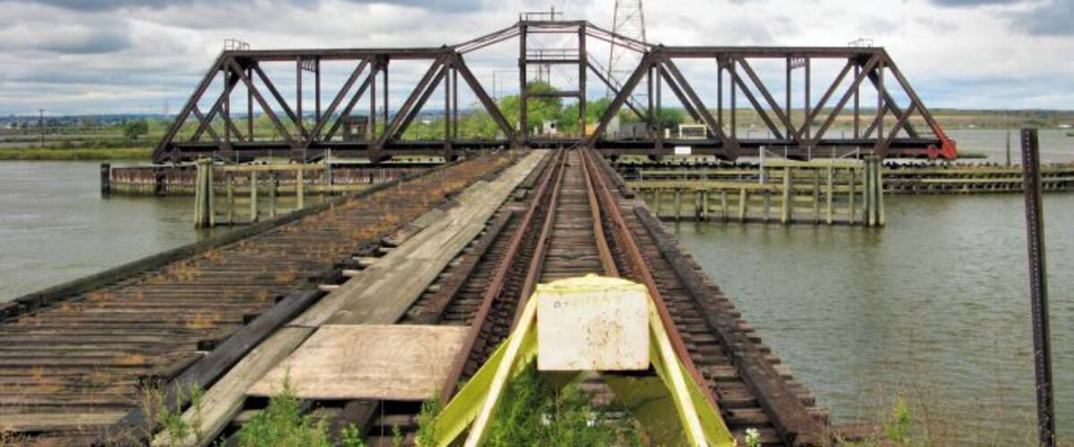 A railway bridge over a body of water with a cloudy sky.