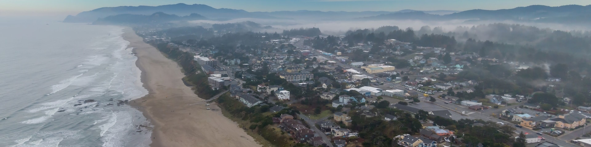Coastal town of Lincoln City shrouded in fog, waves crashing on the beach, hotels and homes line the shore. Aerial view of a misty morning. Oceanlake, Oregon, USA