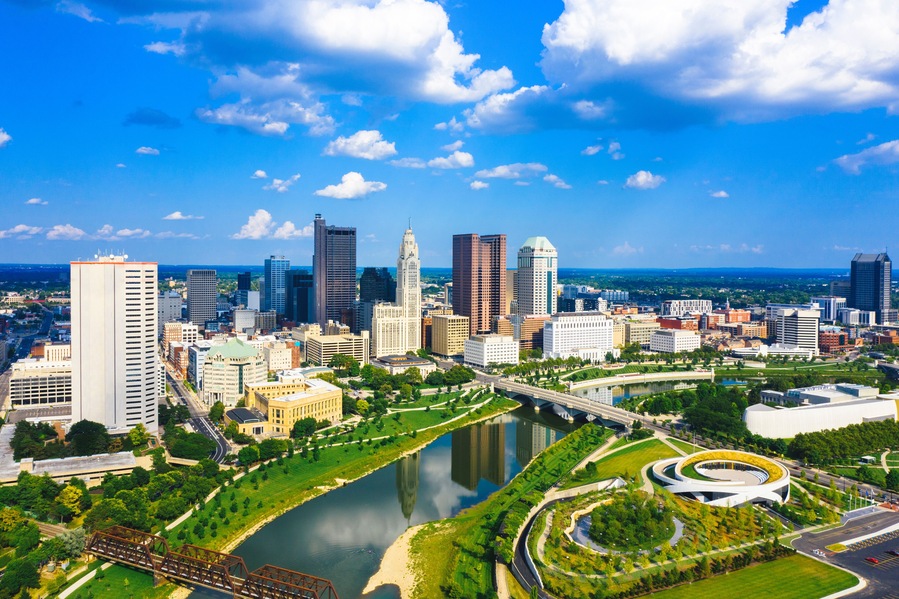 A city skyline with a river, green spaces, and a bridge.