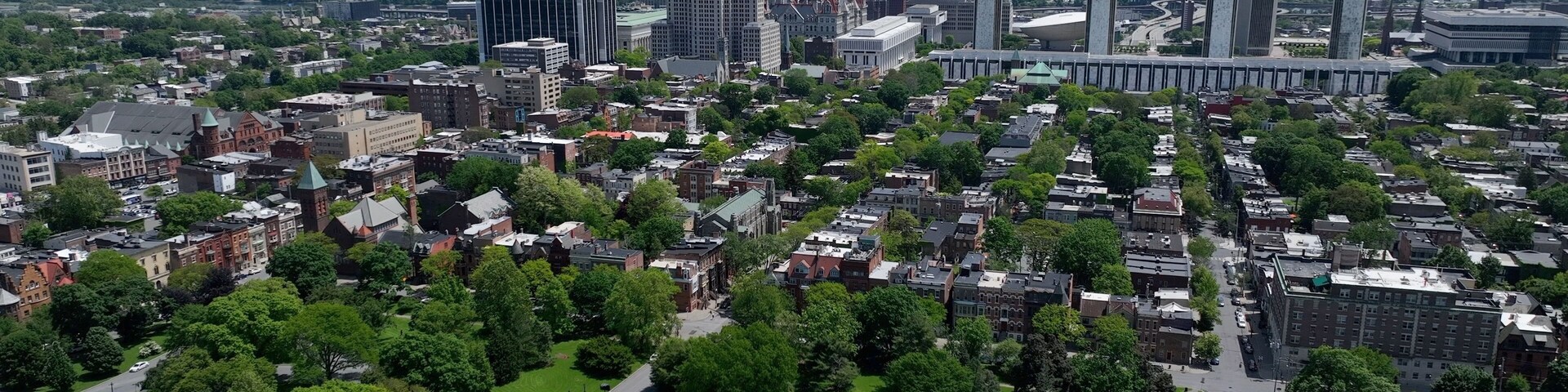 Paisagem urbana com mistura de edifícios modernos e históricos, áreas verdes e vista distante de montanhas.