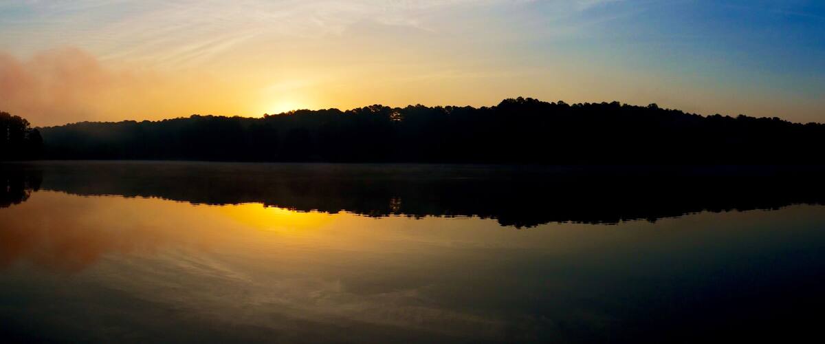 Panoramic view of the rising sun peeks over the foggy horizon at Shelley Lake Park in Raleigh North Carolina.