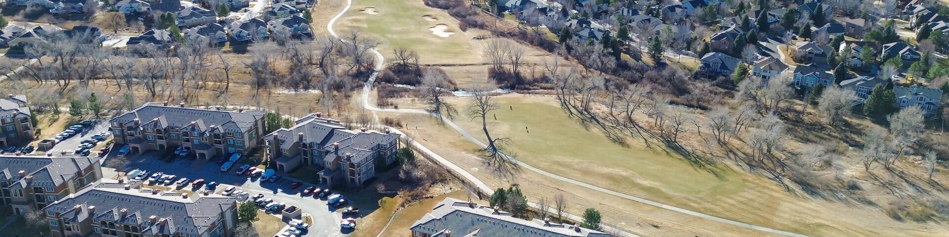 An aerial view of a residential area with houses, a parking lot, and a golf course.