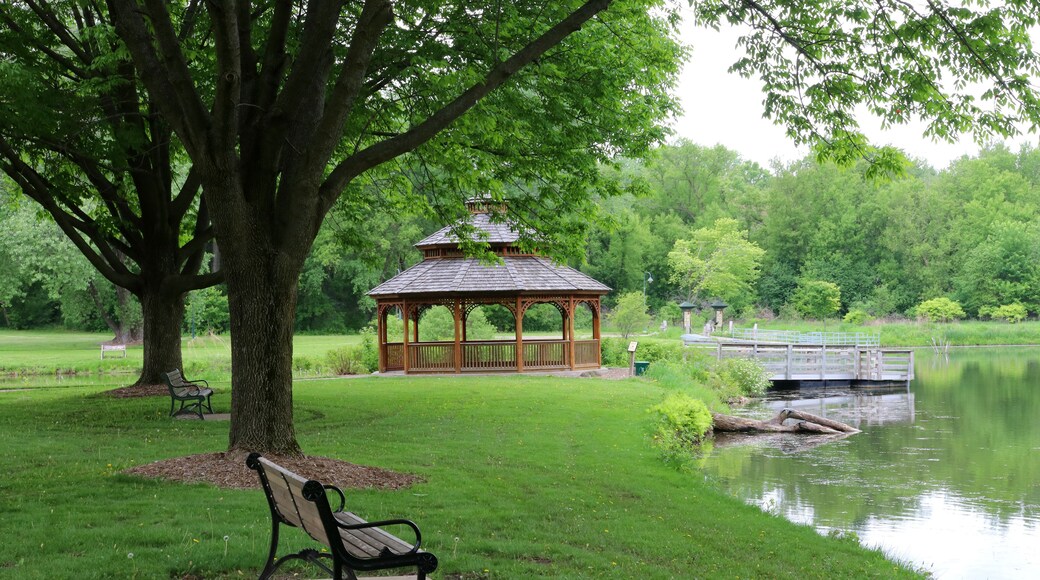 Midwest nature background with city park view.Beautiful late spring landscape with bench in a foreground, trees around the pond and wooden gazebo in a city park.Lakeview park, Middleton, Madison area.