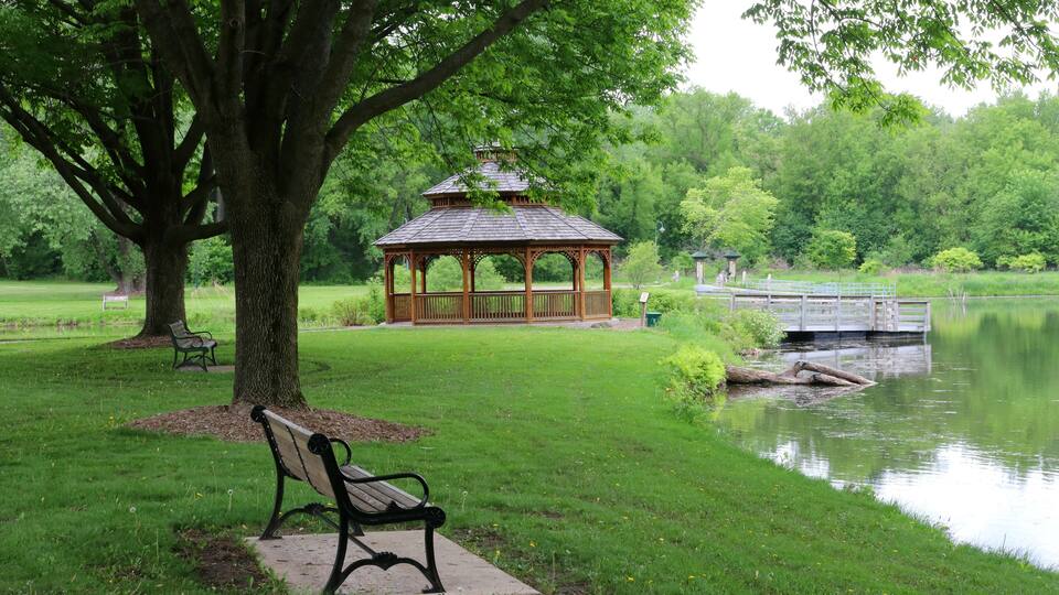 Midwest nature background with city park view.Beautiful late spring landscape with bench in a foreground, trees around the pond and wooden gazebo in a city park.Lakeview park, Middleton, Madison area.