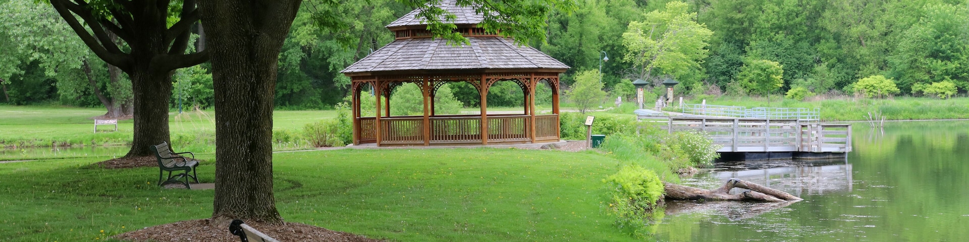 Midwest nature background with city park view.Beautiful late spring landscape with bench in a foreground, trees around the pond and wooden gazebo in a city park.Lakeview park, Middleton, Madison area.