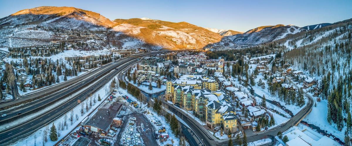 A snow-covered town with a highway, buildings, and mountains in the background.
