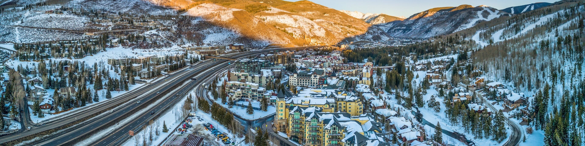 A snow-covered town with a highway, buildings, and mountains in the background.