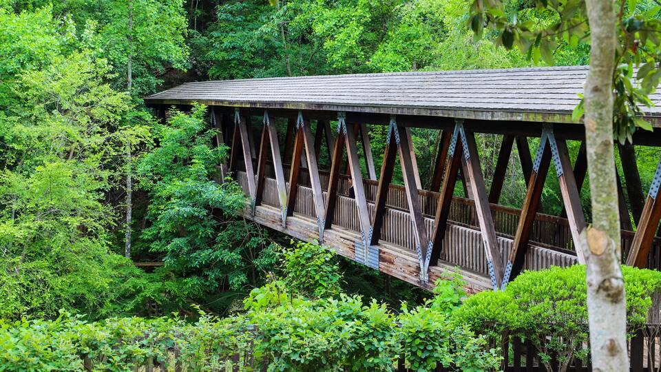 a long covered dark wood bridge over the Big Creek river surrounded by lush green lush green trees at Vickery Creek in Roswell Georgia