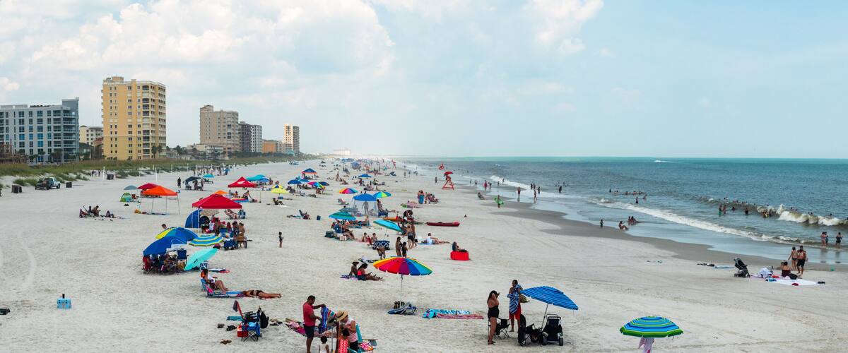 A crowded beach with numerous umbrellas and people.