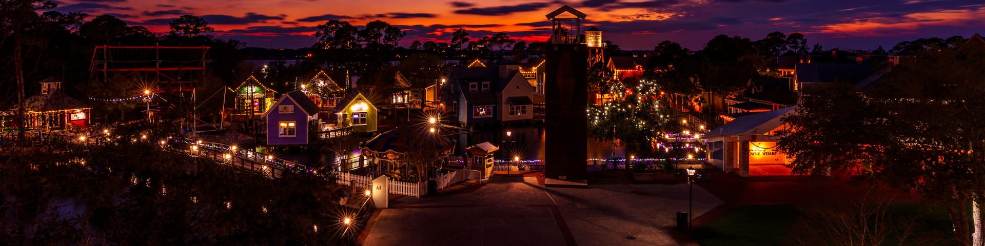 Un pueblo al anochecer con edificios iluminados y un campanario de iglesia destacado.