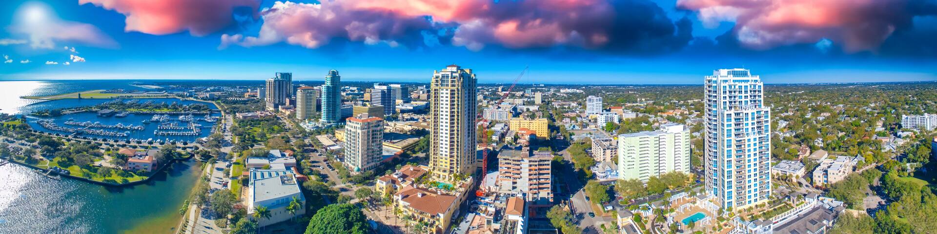 A coastal cityscape with high-rise buildings, a marina, and a clear blue sky.