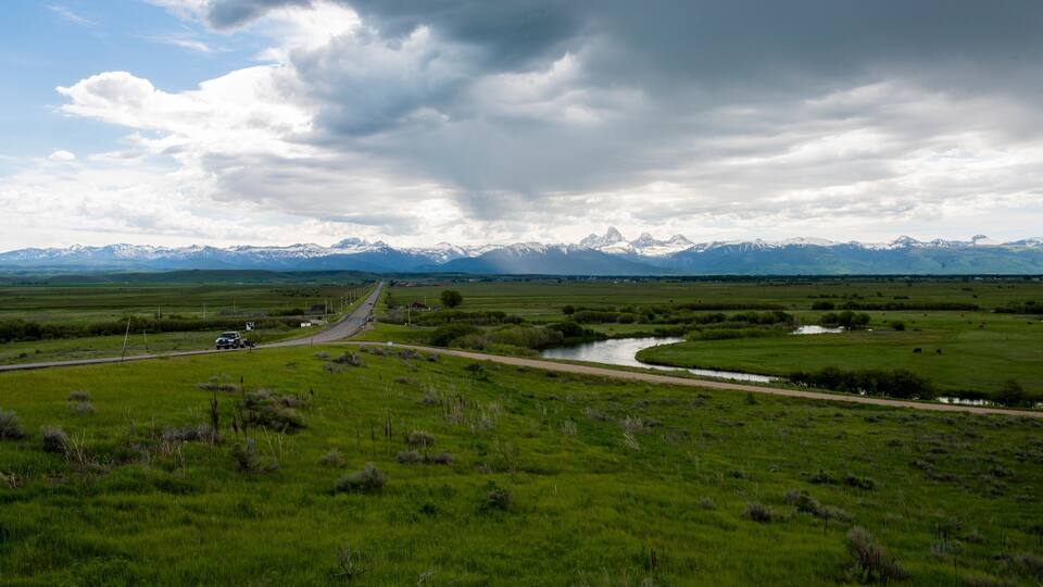 A view of the Teton mountains from several miles north of Victor, Idaho, with green agricultural fields and interesting clouds overhead
