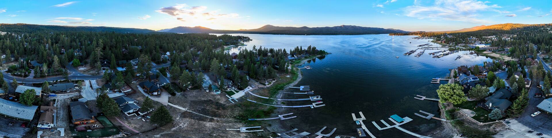 A panoramic view of a lake surrounded by dense forests and mountains, with a marina and residential areas along the shore.