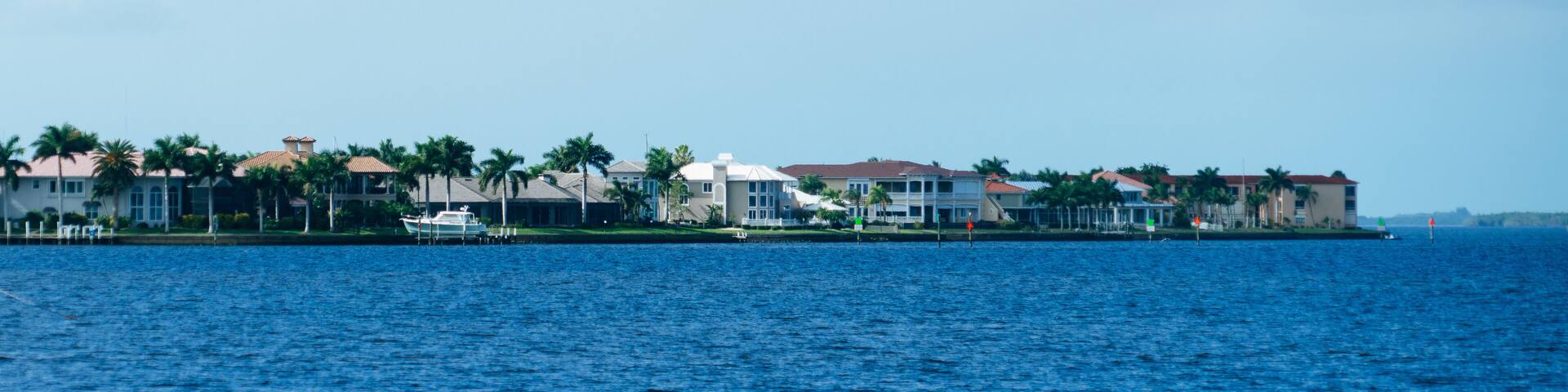 A coastal residential area with houses, palm trees, and a boat docked near the water.