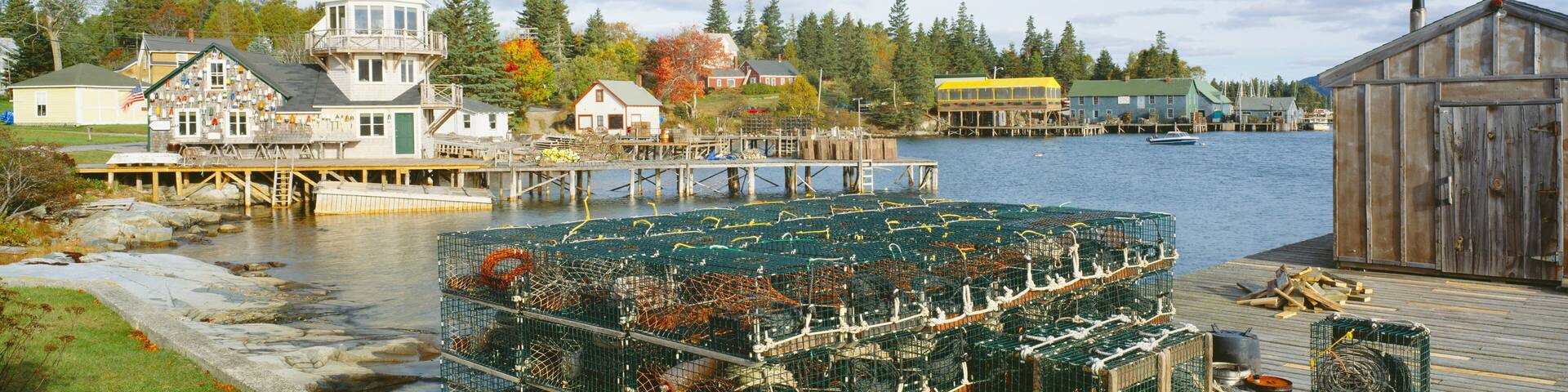 A coastal town with a lighthouse, wooden docks, and a large lobster trap.
