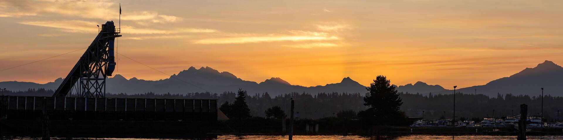 A sunset over mountains with a bridge and dock in the foreground.
