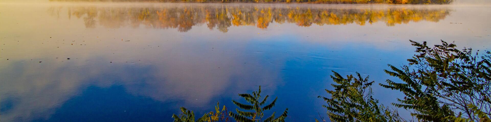 A calm lake with autumn-colored trees reflecting on the water's surface.