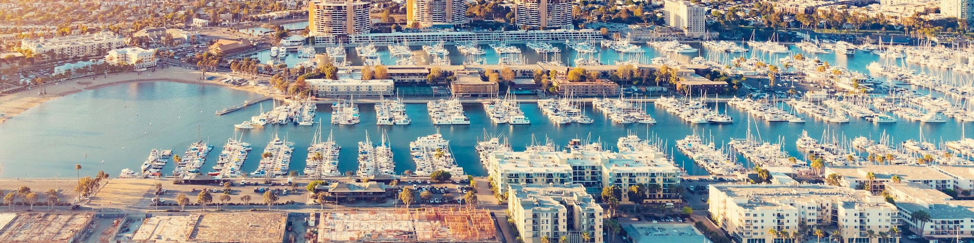 Uma marina com vários barcos atracados, cercada por edifícios urbanos e uma grande extensão de água.