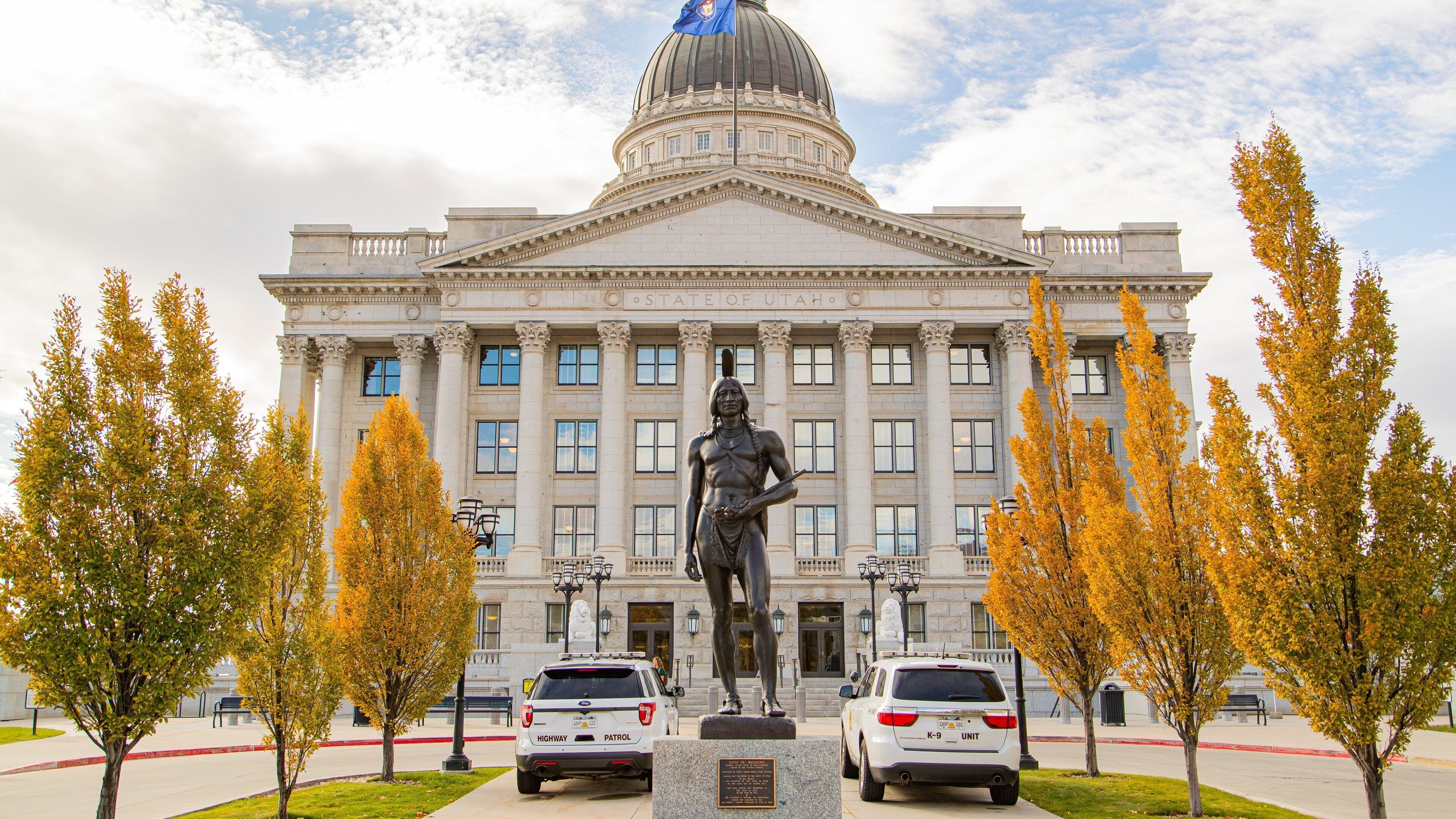 A large neoclassical building with a dome, flanked by two statues and two police cars in front.