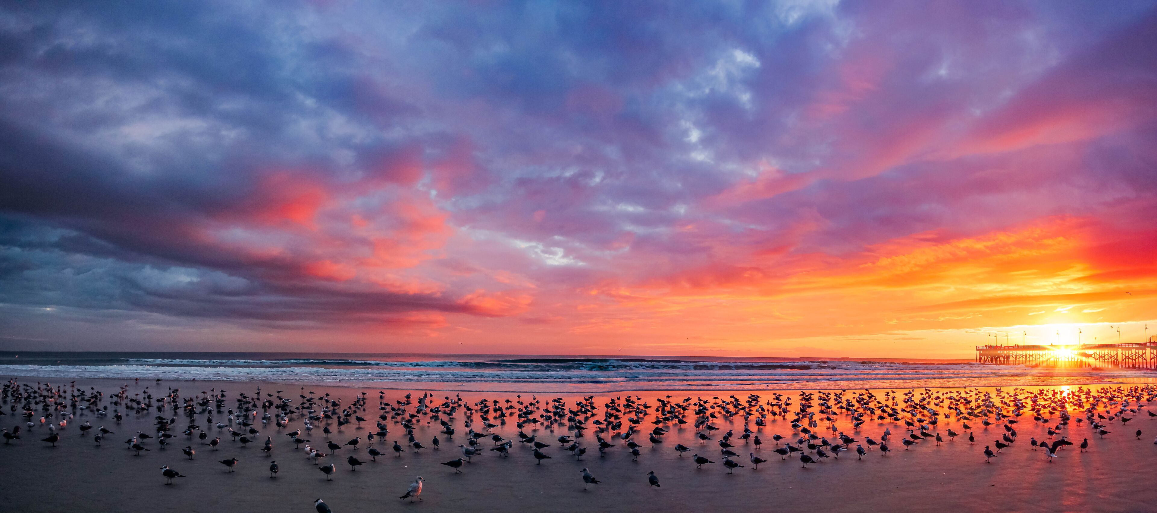 A beach at sunset with a pier in the background.