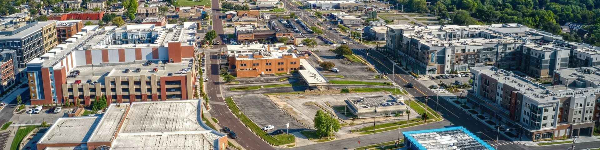 An aerial view of a city with a mix of commercial and residential buildings, a large parking lot, and a water tower in the distance.