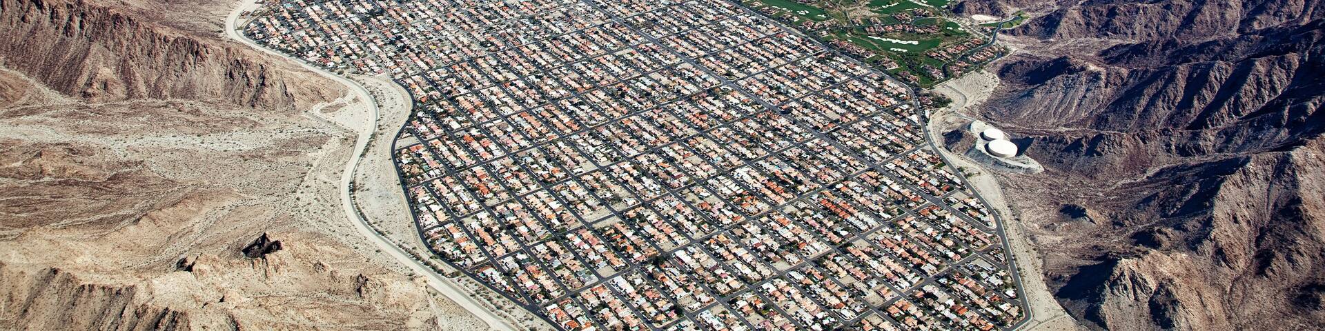 An aerial view of a city with a grid layout, surrounded by mountains and valleys.