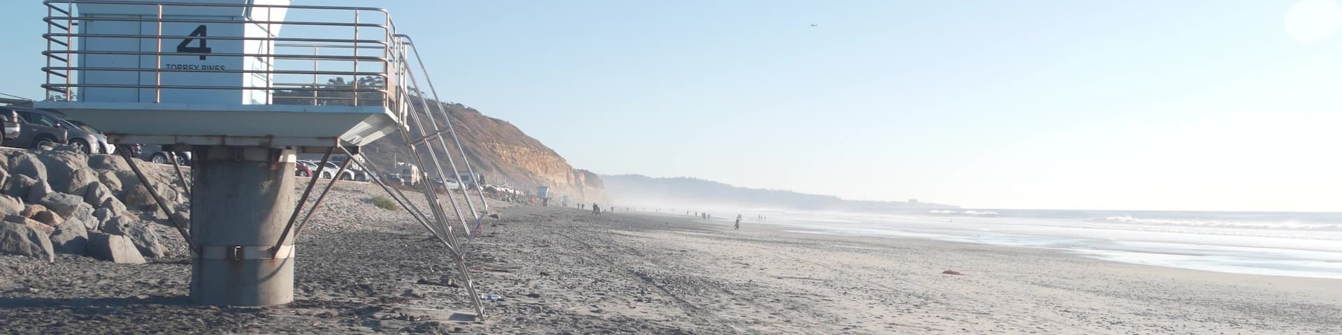 Steep cliff, rock or bluff, California coast erosion, Del Mar, San Diego, USA. People walking along eroded crag. Torrey Pines state beach, ocean water waves. Lifeguard tower, life guard station or hut