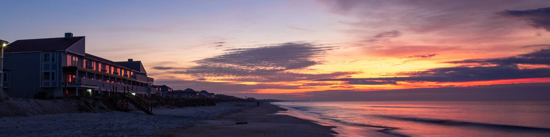 A beach at sunset with a row of houses along the shore.