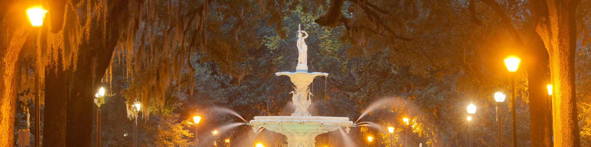 A park with a fountain, benches, and trees with hanging moss.