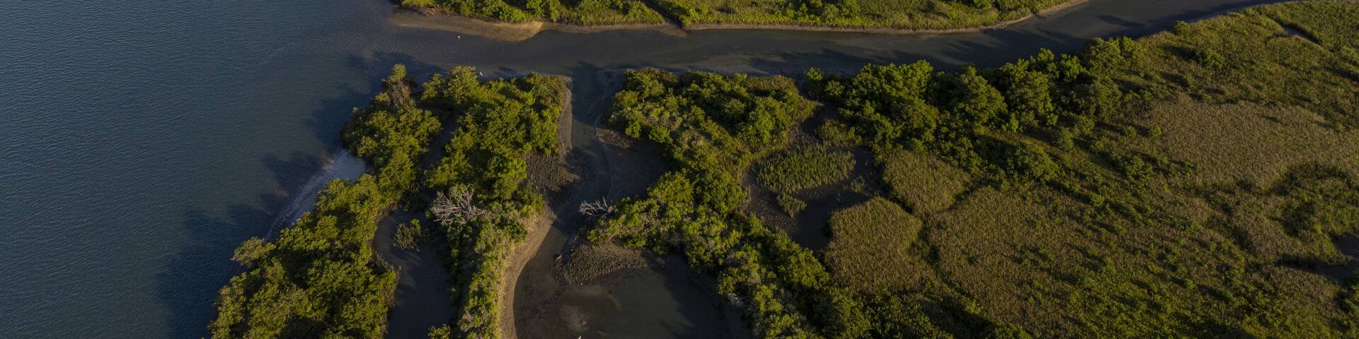 Aerial view of the Matanzas River snaking through the marshland, a tapestry of greens and blues, where water meets land in a dance of light and shadow, St Augustine, Florida, United States.