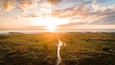 Un coucher de soleil sur un champ d’herbe, avec un sentier qui mène à l’eau.