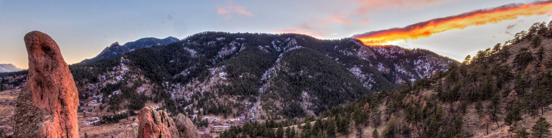 A rugged mountain landscape with prominent red rock formations and a dense forest.