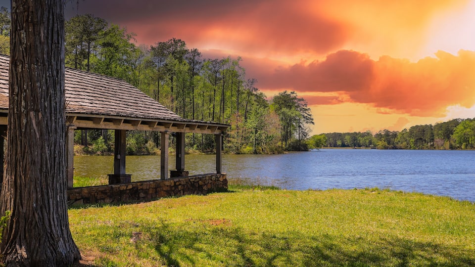 A gazebo by a lake with a sunset sky.