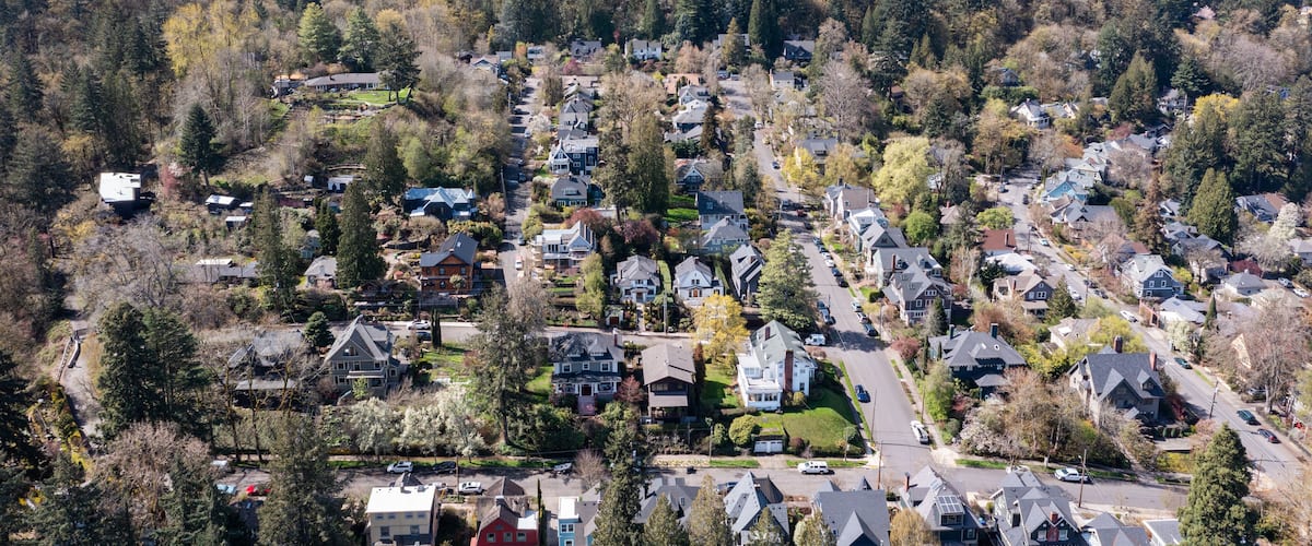 Aerial drone view of Northwest Portland, Oregon, showing Forest Park, Nob Hill, and Willamette Heights with greenery, homes, and industrial areas along the Willamette River