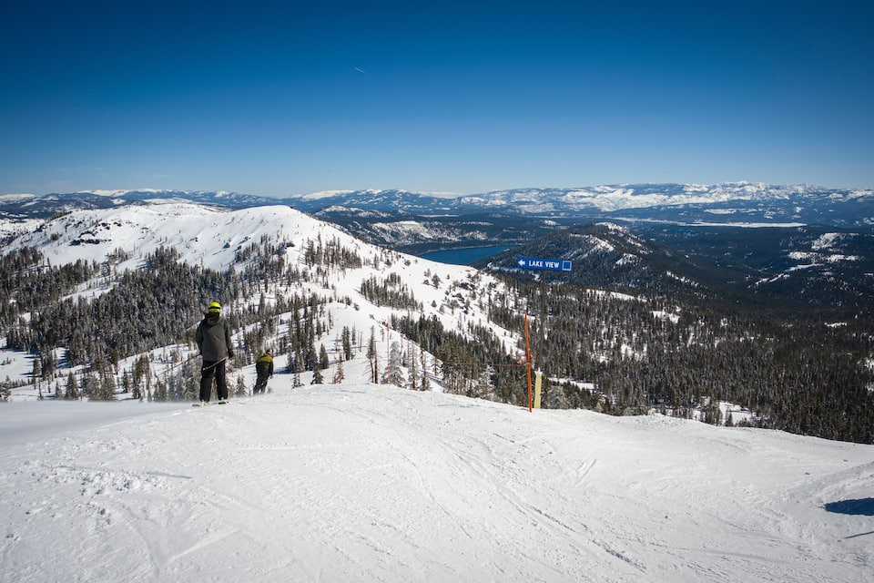A snowy mountain landscape with a ski slope, a ski lift, and a lake in the distance.