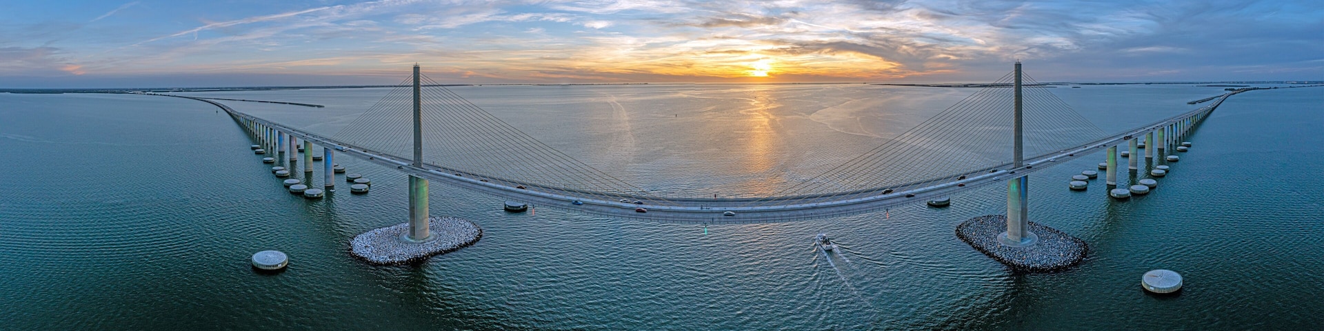 A large suspension bridge over calm water with a sunset in the background.