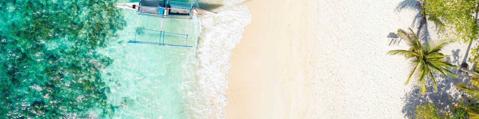 View from above, stunning aerial view of a Bangka boat in front of a white sand beach bathed by a turquoise water. Coron Island, Palawan, Philippines.