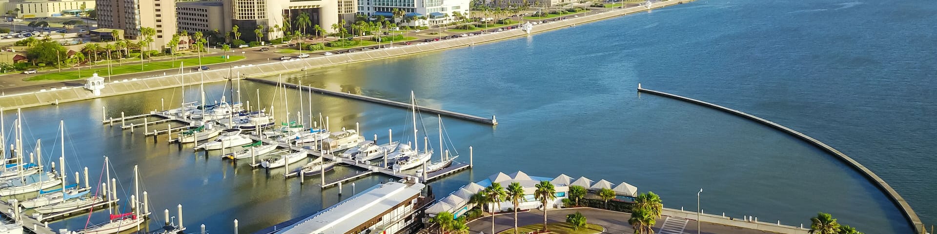 Panorama aerial view Bayfront area of Corpus Christi with skylines and marina piers row of boat, sailboat and yacht at sunrise. City harbor bridge far right in distance. A Texas city on Gulf of Mexico