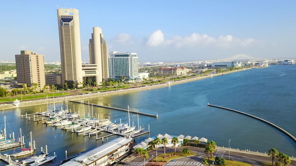 Panorama aerial view Bayfront area of Corpus Christi with skylines and marina piers row of boat, sailboat and yacht at sunrise. City harbor bridge far right in distance. A Texas city on Gulf of Mexico