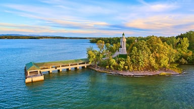 A wooden pier extending into a lake, surrounded by lush greenery and a prominent lighthouse on a small island.